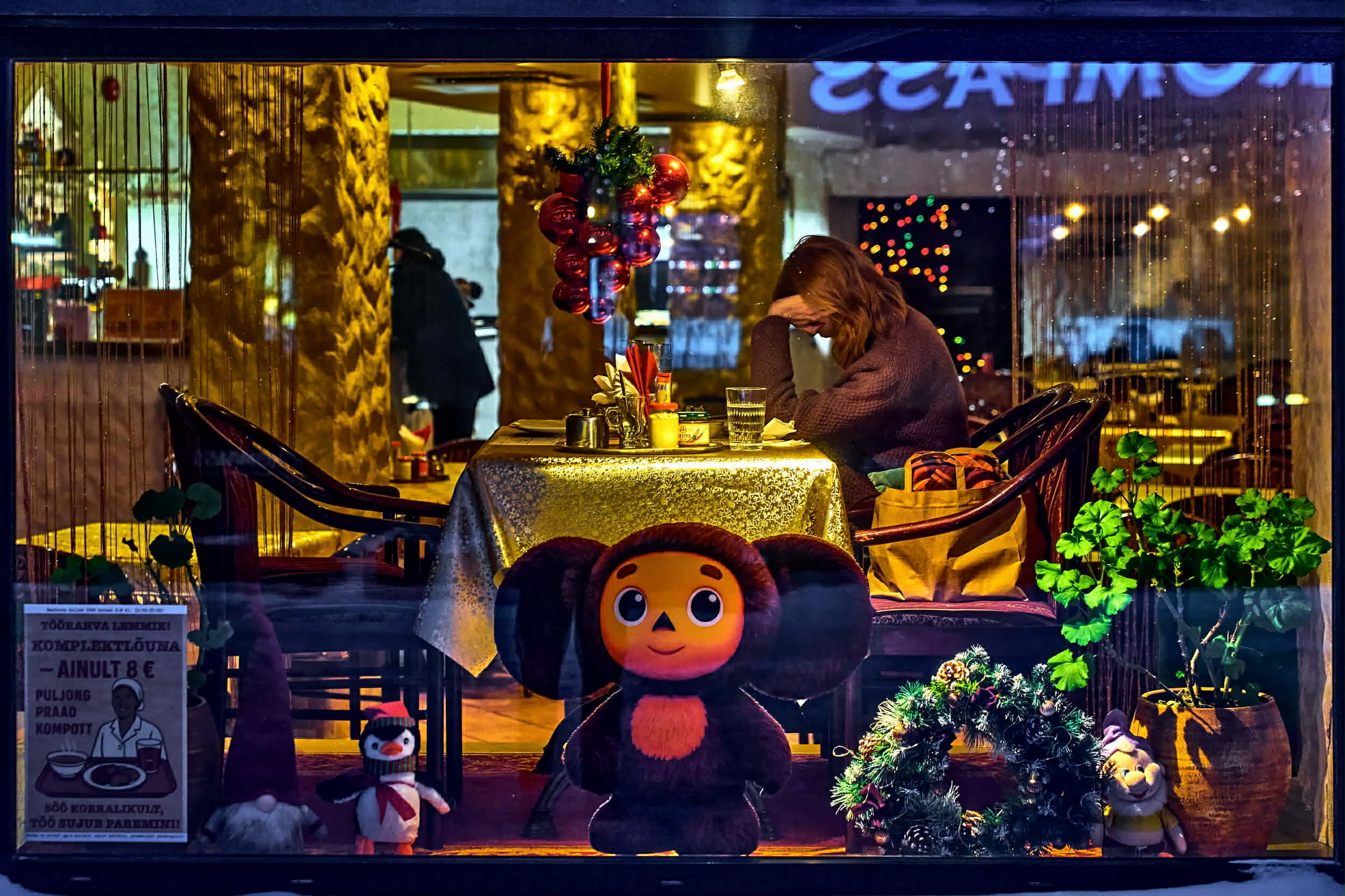 A beautifully arranged wooden table is laden with an assortment of foods, including baskets of bread, trays of pies, and plates of fried items. Soft, warm lighting is provided by string lights and candles, creating a cozy atmosphere. Incorporating natural and elegant elements, there is also some decorative foliage.